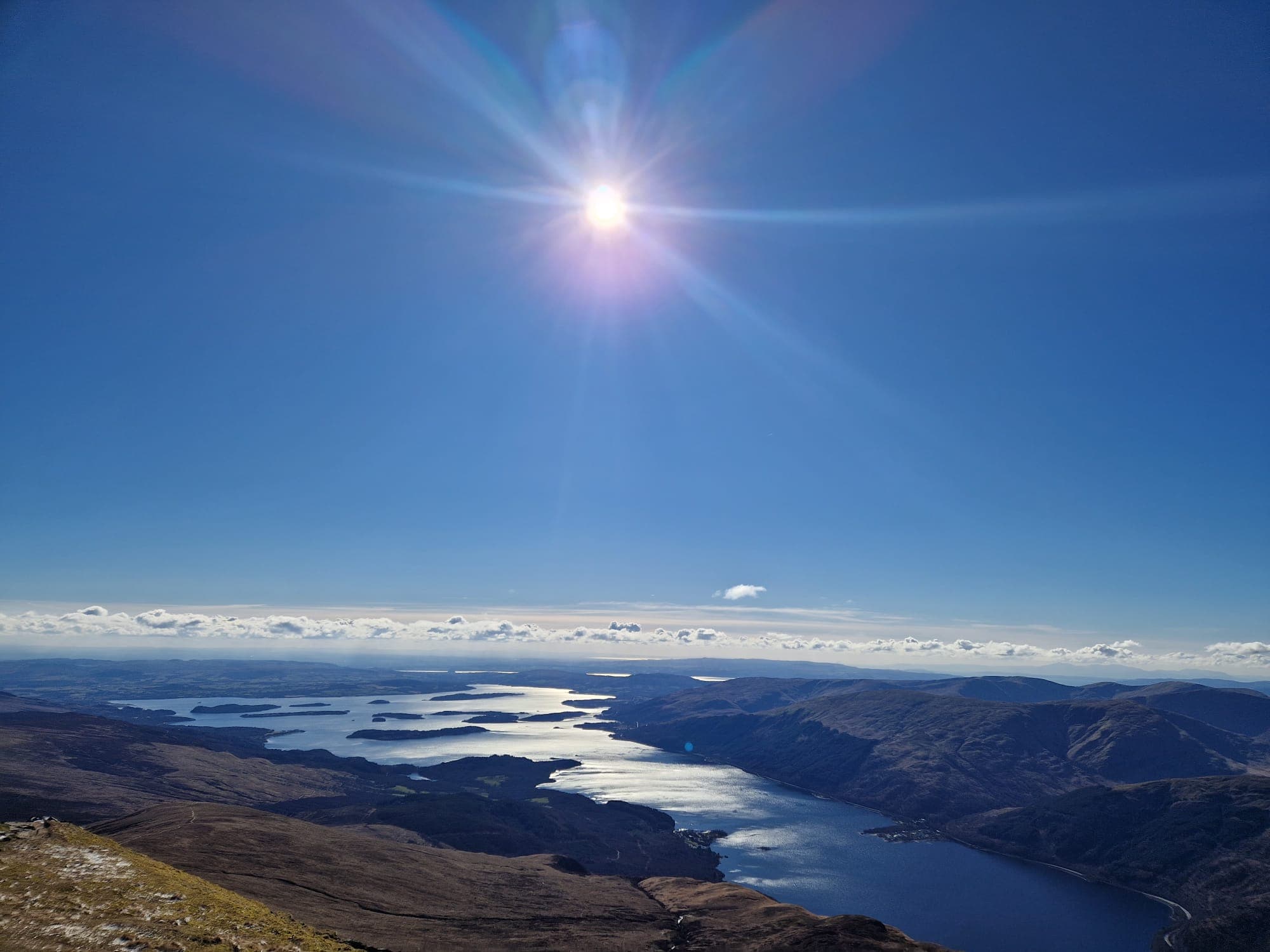 View from the summit of Ben Lomand, with clear blue skies and the sun shining across Loch Lomand.